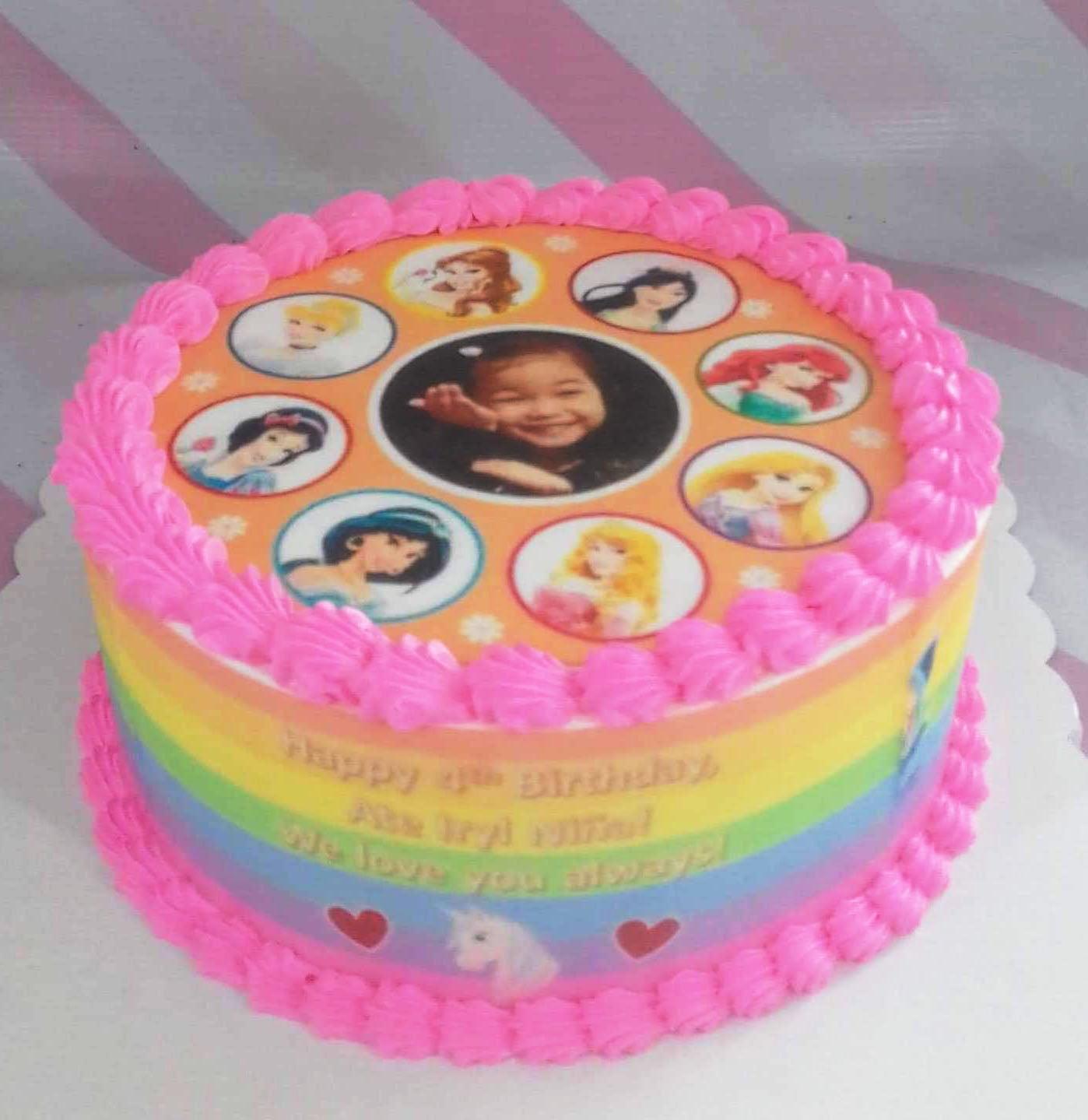 Rainbow princess birthday cake with pink icing borders and printed Disney princess characters and a photo of a young girl.