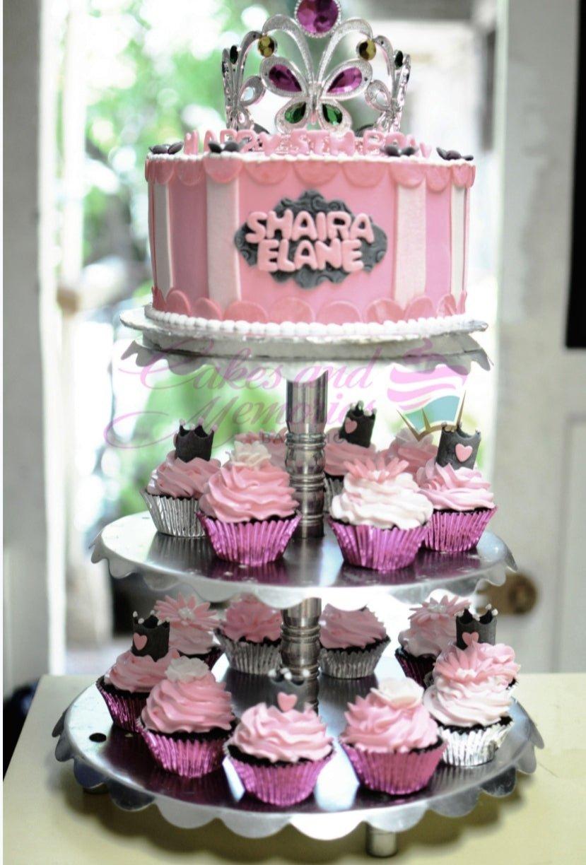Pink and white striped princess cake with a silver tiara topper and matching cupcakes on a silver stand.