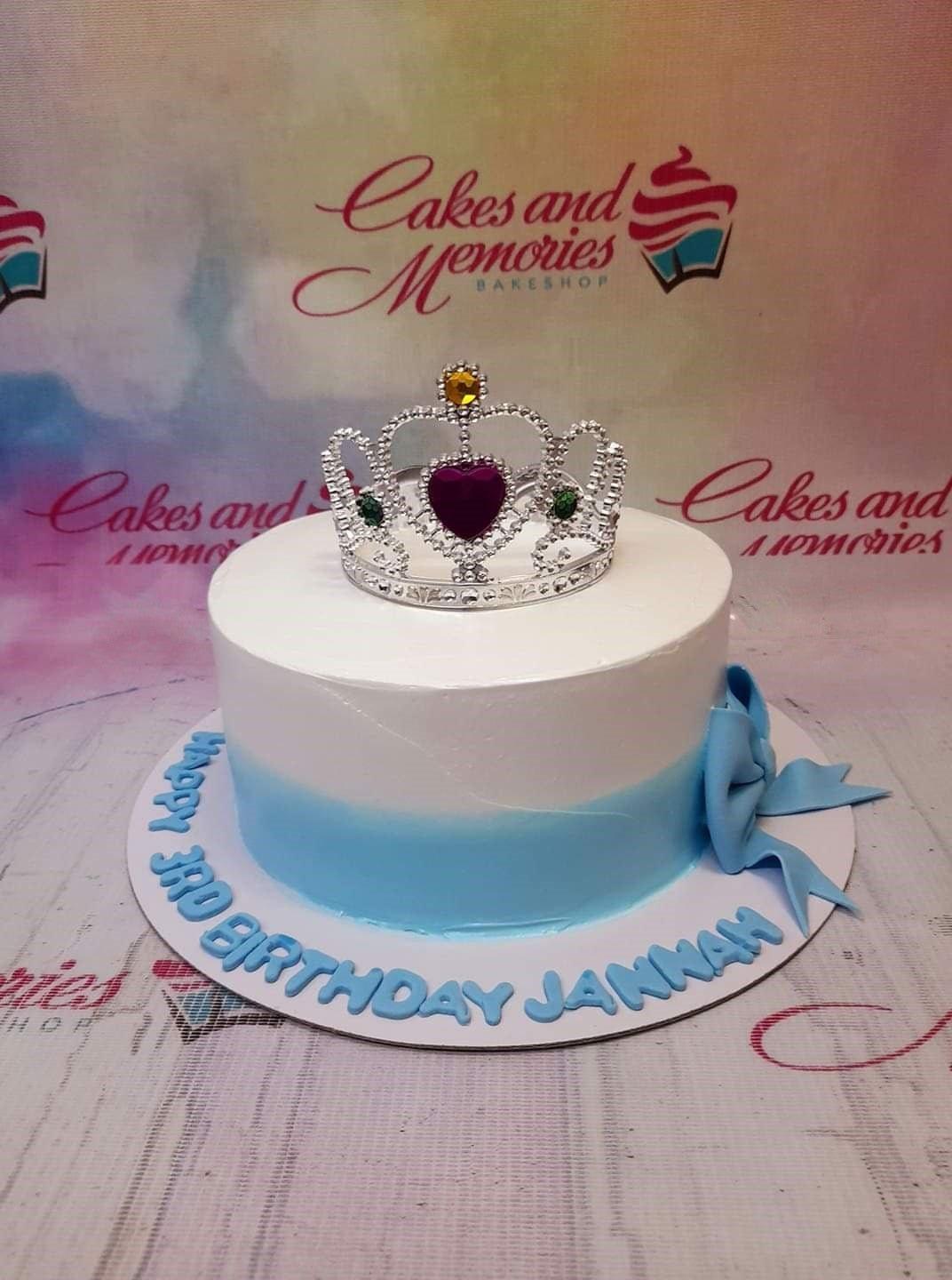 White and light blue gradient cake with a silver rhinestone tiara and a blue fondant bow on the side.