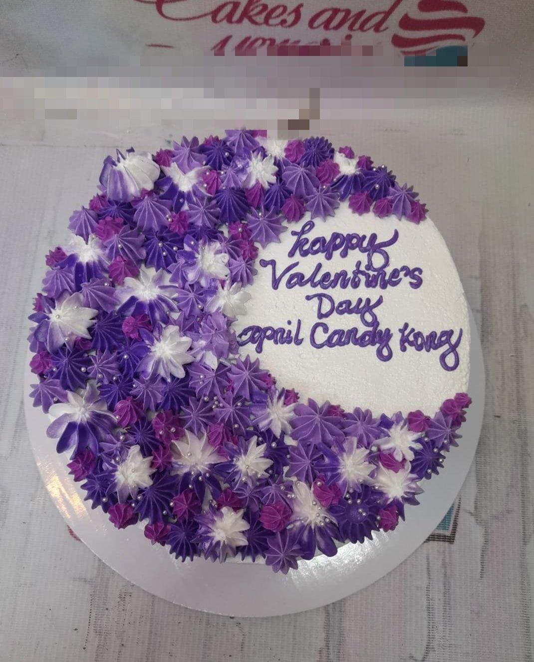 Round white cake with a crescent moon design made of purple and white icing rosettes and silver dragees.