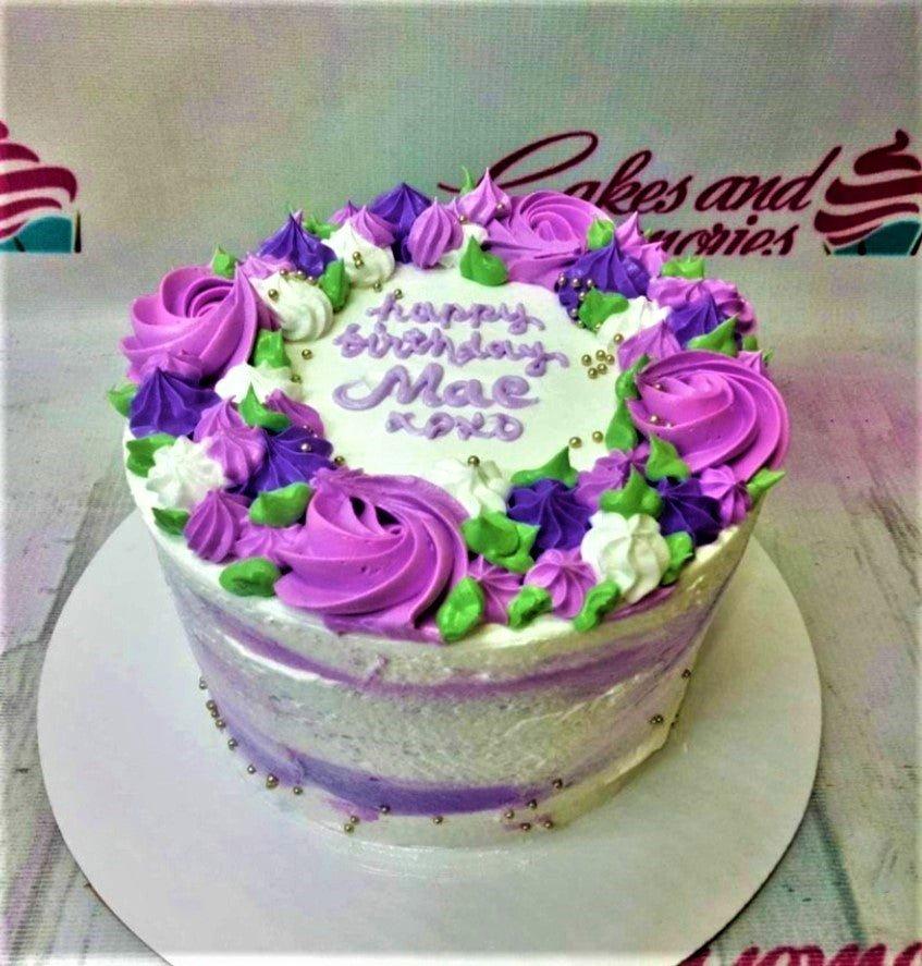 Single tier white cake with purple and green icing rosettes and gold dragees featuring a Happy Birthday Mae message.