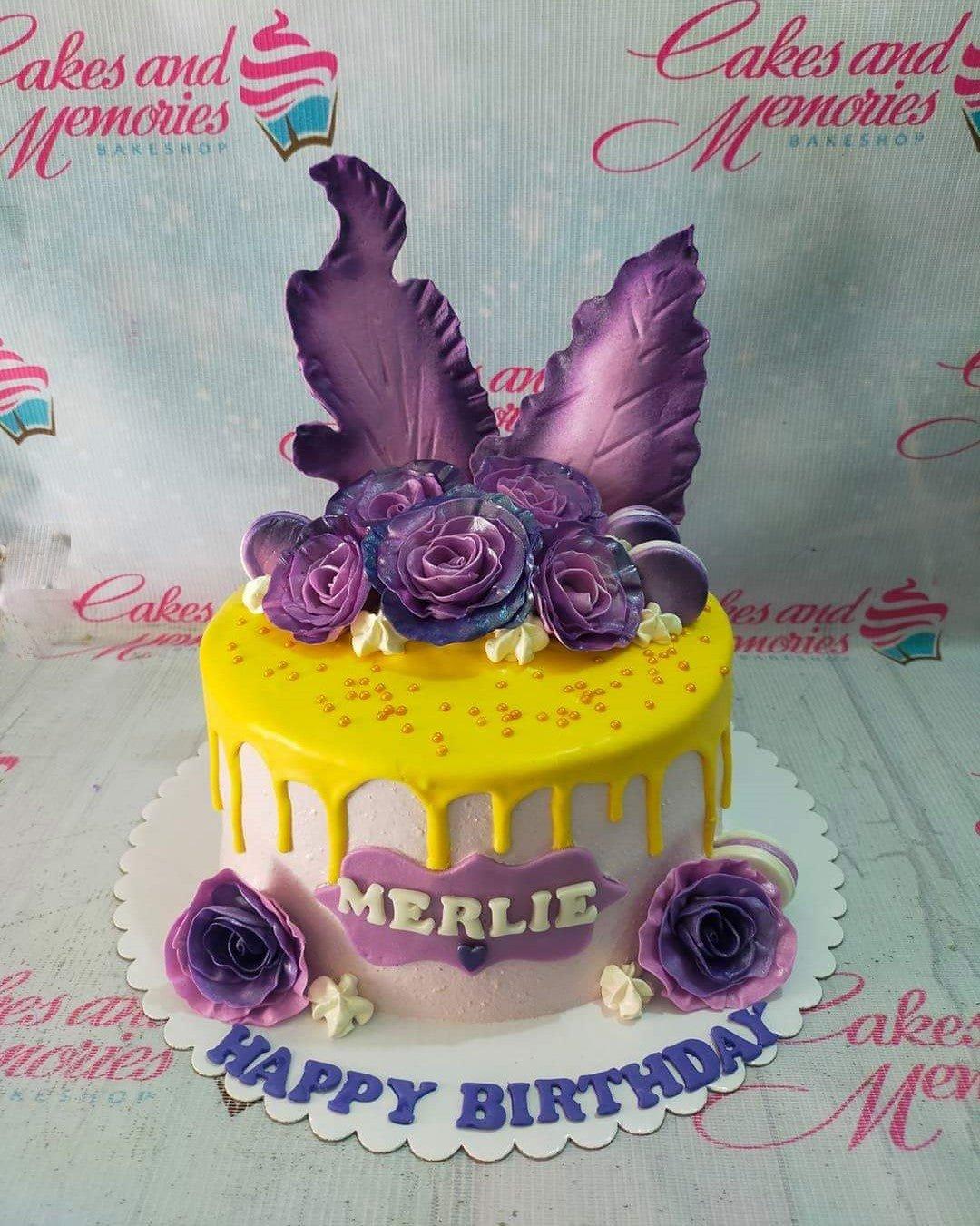 Purple and yellow birthday cake with large gumpaste roses, purple leaf toppers, and yellow drip icing.