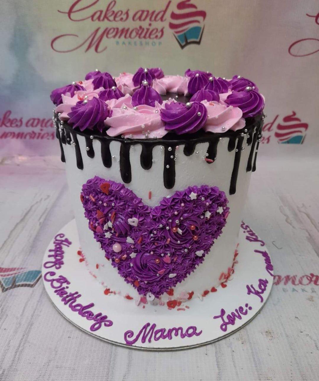 White 1-tier birthday cake with chocolate drip, purple and pink icing rosettes, and a large purple piped icing heart on the side.
