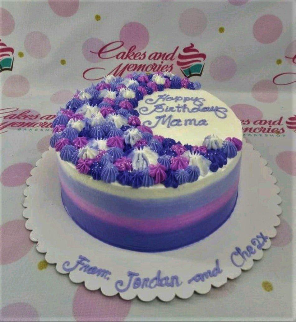 A round birthday cake with purple and pink gradient icing, topped with a crescent of purple, pink, and white icing rosettes and sprinkles.