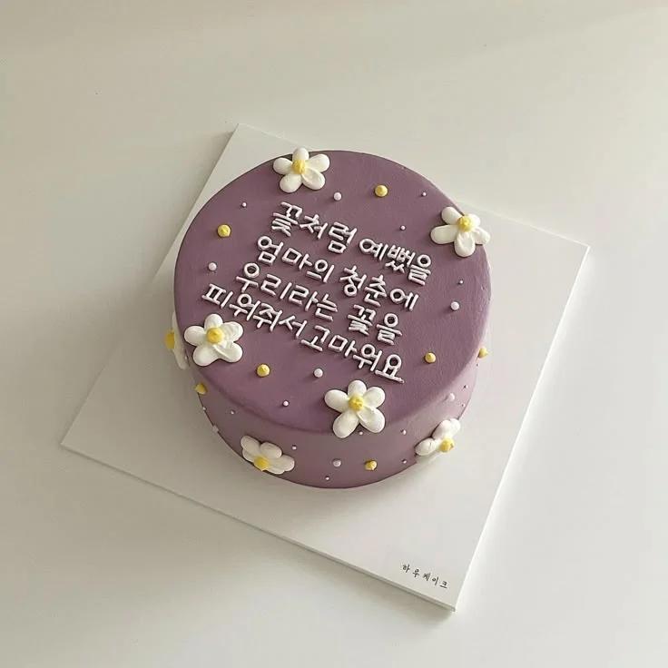 Purple minimalist cake with white icing flowers and yellow centers, featuring a long Korean message in white icing text.