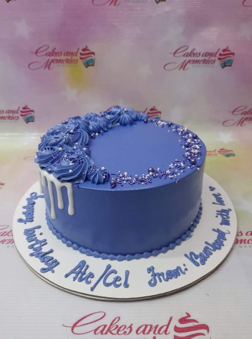 Single tier purple birthday cake with blue icing rosettes, white chocolate drip, and purple and white sprinkles on a white base board.