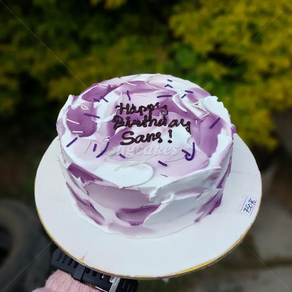 A bento cake with white and purple palette knife icing, purple sprinkles, and a 'Happy Birthday Sans!' message in dark brown icing.