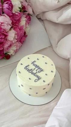 White bento cake with purple piped 'happy birthday' message and small purple heart icing decorations on a white cake board.