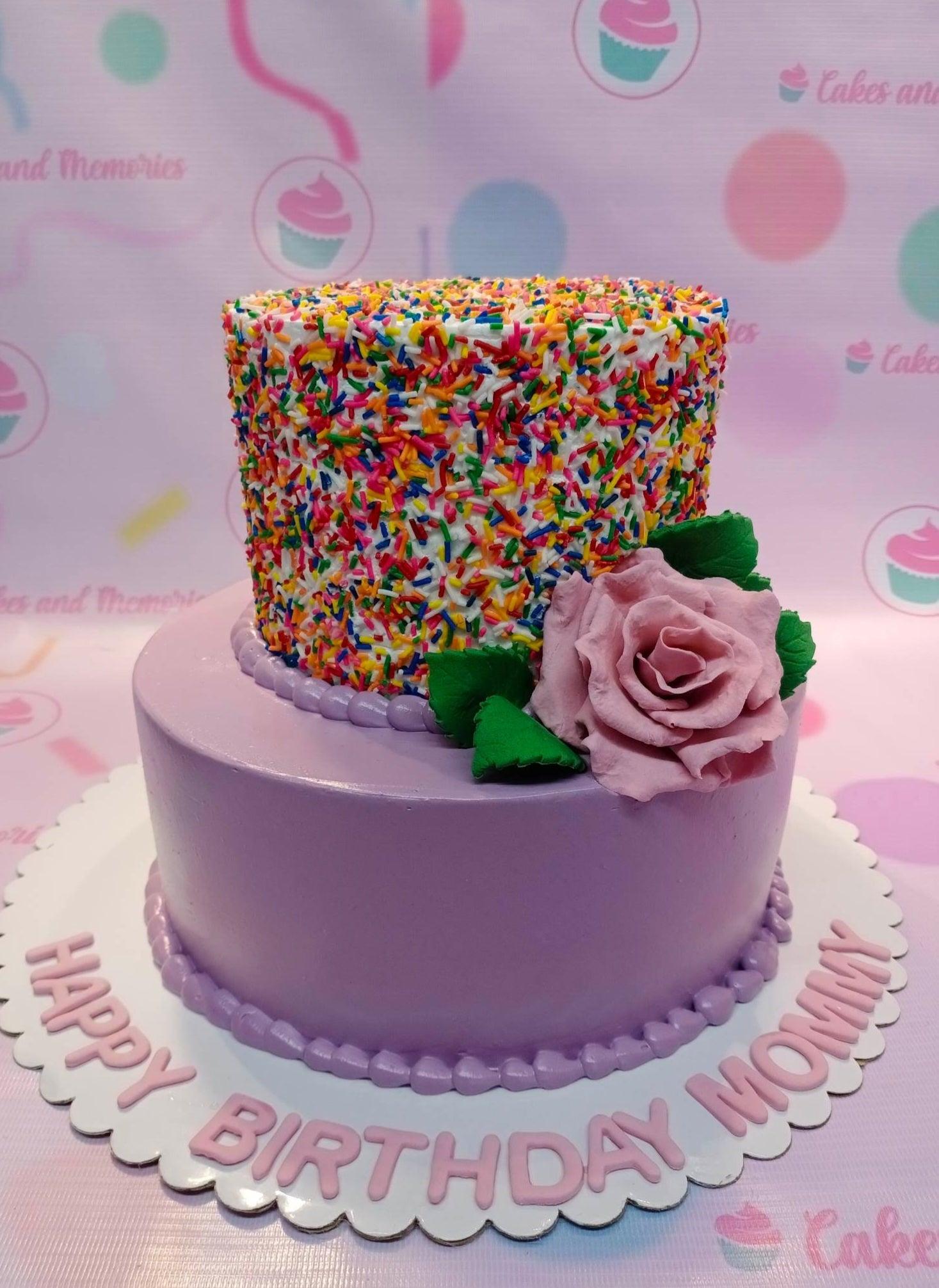 Two-tier purple birthday cake with a sprinkle-covered top tier and a large pink fondant rose accent.