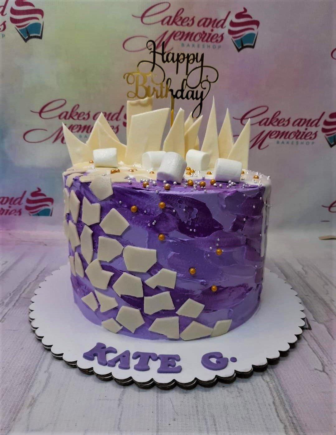Purple and white textured icing cake with white chocolate shards, marshmallows, and a gold Happy Birthday topper.