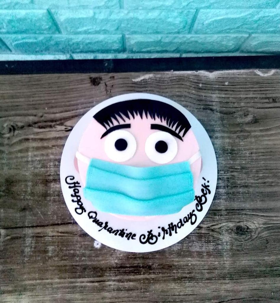 Quarantine themed birthday cake featuring a face with a blue surgical mask and black hair on a white base.