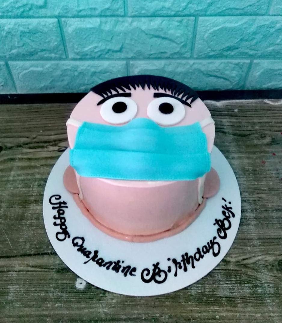Pink quarantine birthday cake featuring a face with a blue surgical mask and black hair, with a message on the base board.