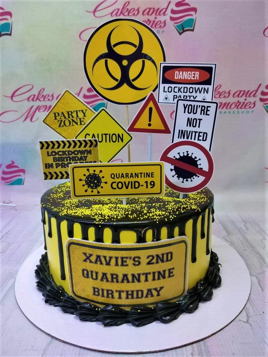 Yellow and black quarantine themed birthday cake with biohazard and caution sign toppers and chocolate drip.