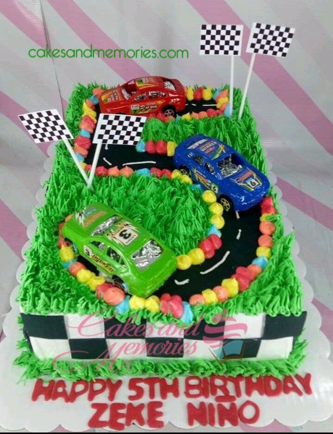 Race car themed rectangle cake with green grass icing, a black racetrack, and three toy cars in red, blue, and green.