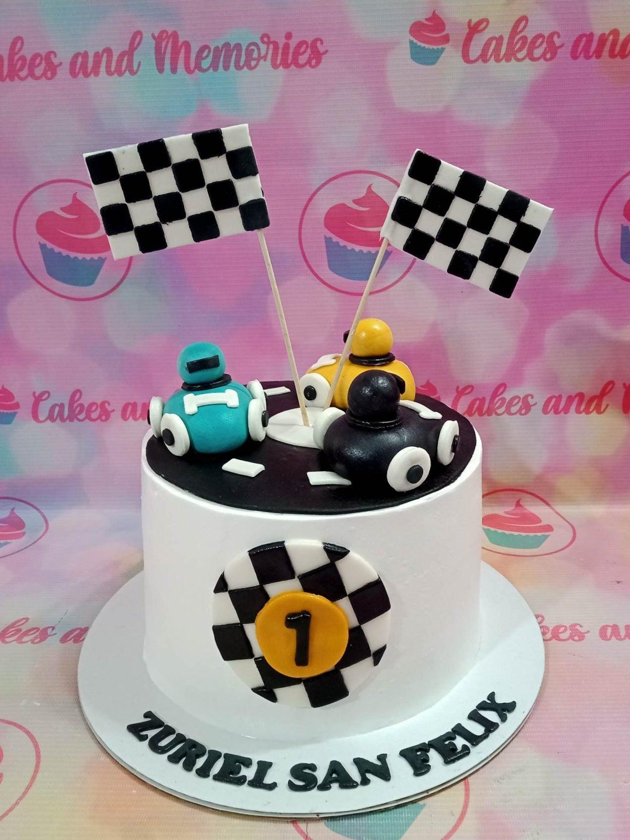 White racing car themed birthday cake with checkered flags and fondant race cars on a black track top.