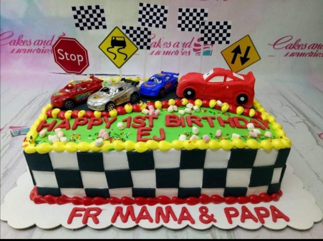 Rectangle racing car birthday cake with checkered flag pattern, toy cars, and green icing grass for a 1st birthday.