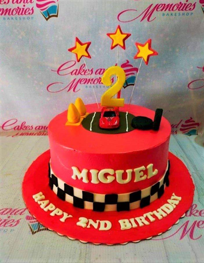 Red racing car themed birthday cake with a checkered flag border, toy car topper, and yellow stars for a 2nd birthday.