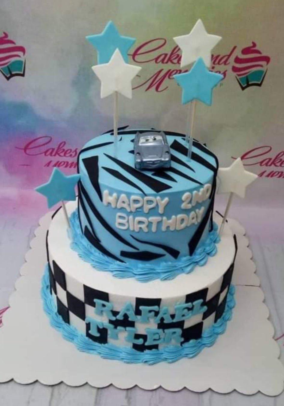 Two-tier blue and white racing themed cake with a toy car topper, stars, and checkered pattern.