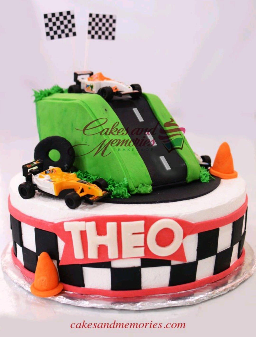 Racing car themed cake with a green hill, black road, and toy race cars on a checkered base.