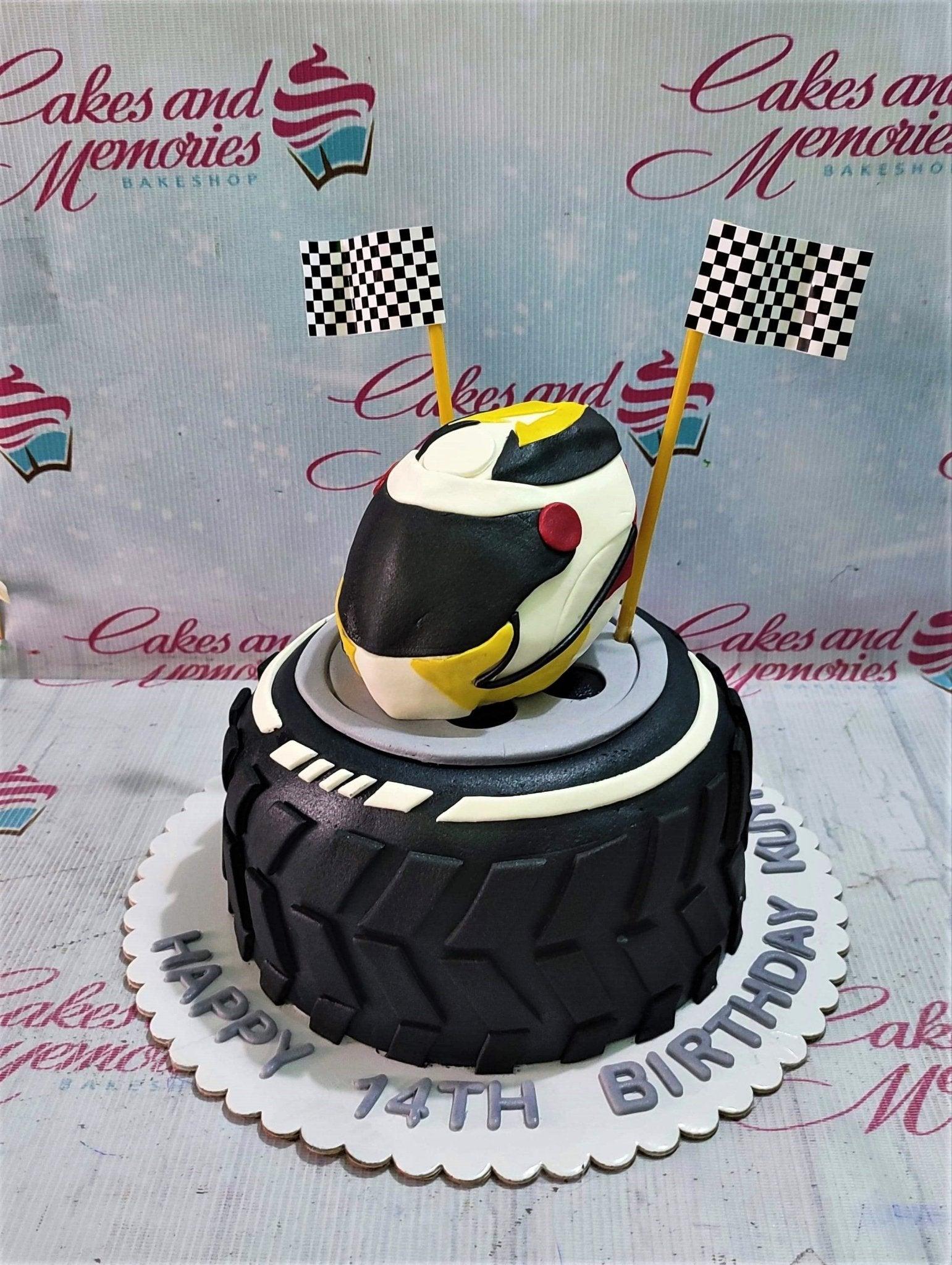 A black tire-shaped fondant cake with a racing helmet topper and checkered flags for a 14th birthday.