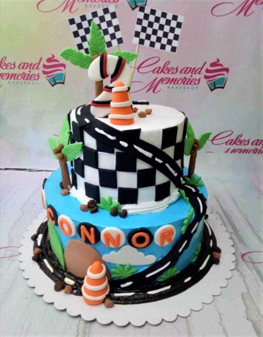 Two-tier racing themed birthday cake with checkered patterns, race tracks, and palm trees for Connor's 2nd birthday.