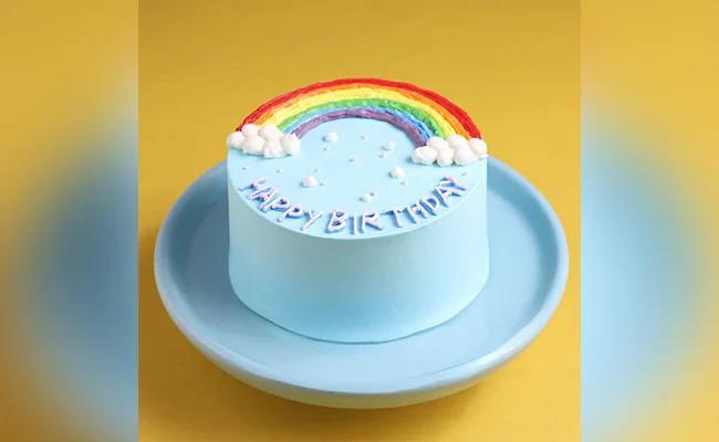 Light blue bento cake with a piped rainbow and clouds on top and Happy Birthday message on the side.