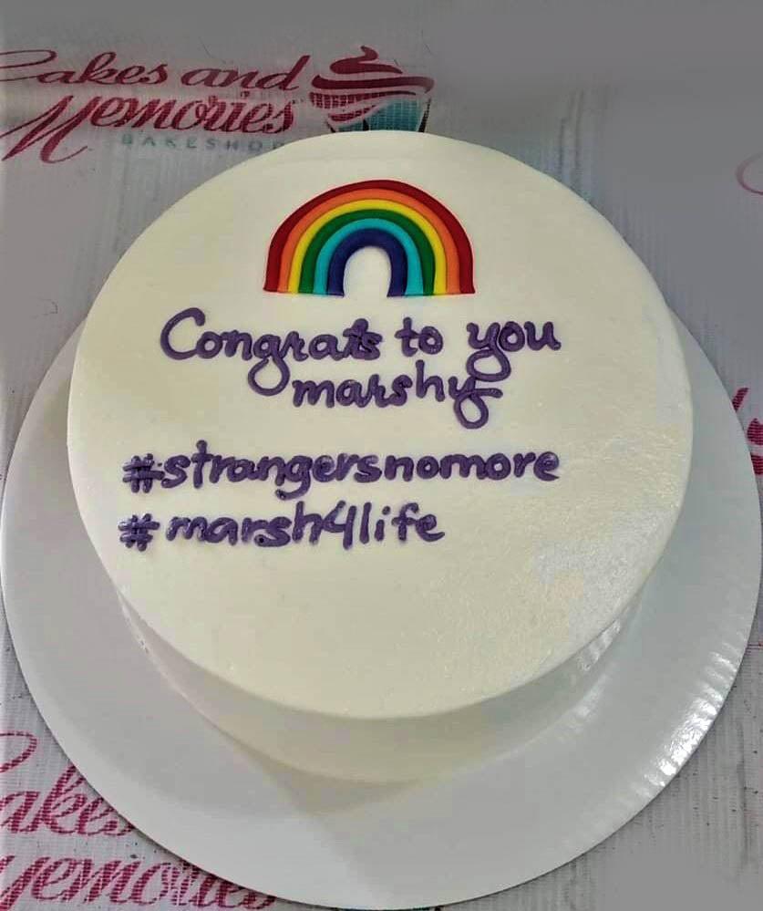White bento cake with a colorful rainbow printout and purple piped icing message on top.