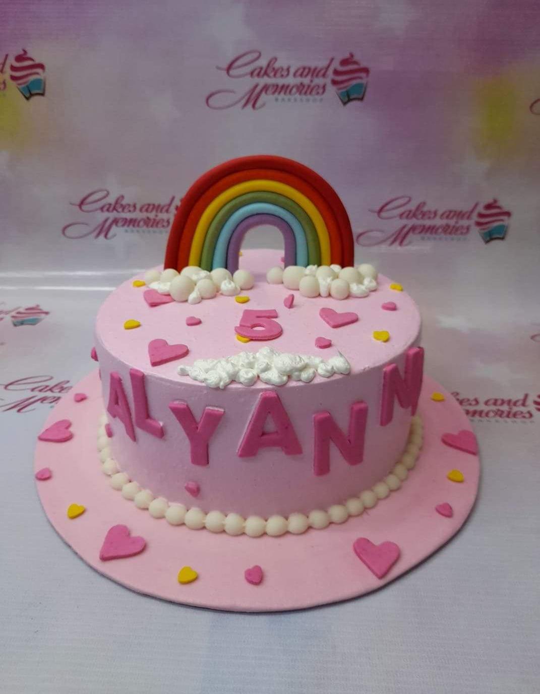 Pink rainbow birthday cake for Alyann's 5th birthday with fondant hearts, clouds, and a colorful rainbow topper.