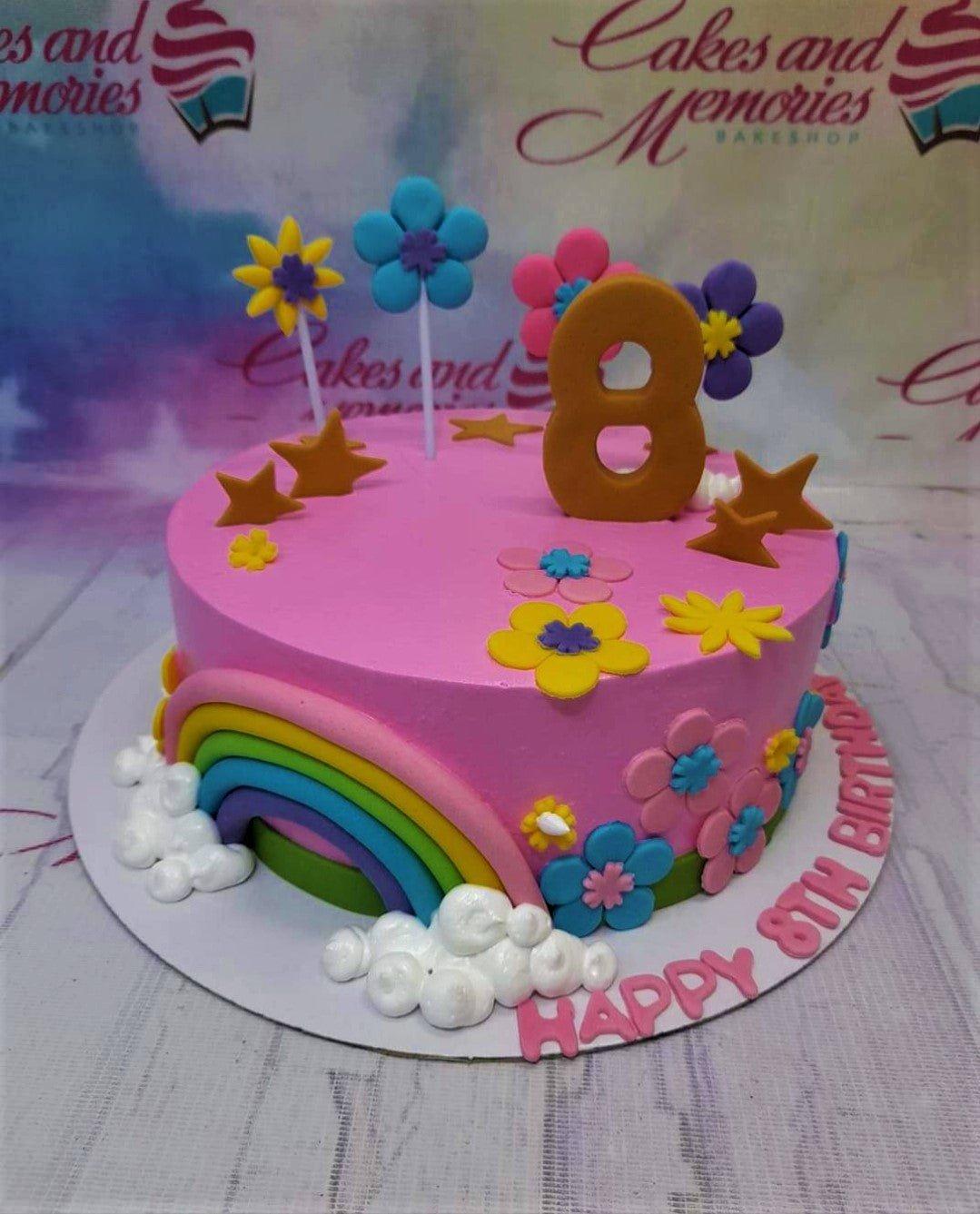 Pink 1-tier birthday cake with a fondant rainbow, clouds, colorful flowers, and a large gold number 8 topper.