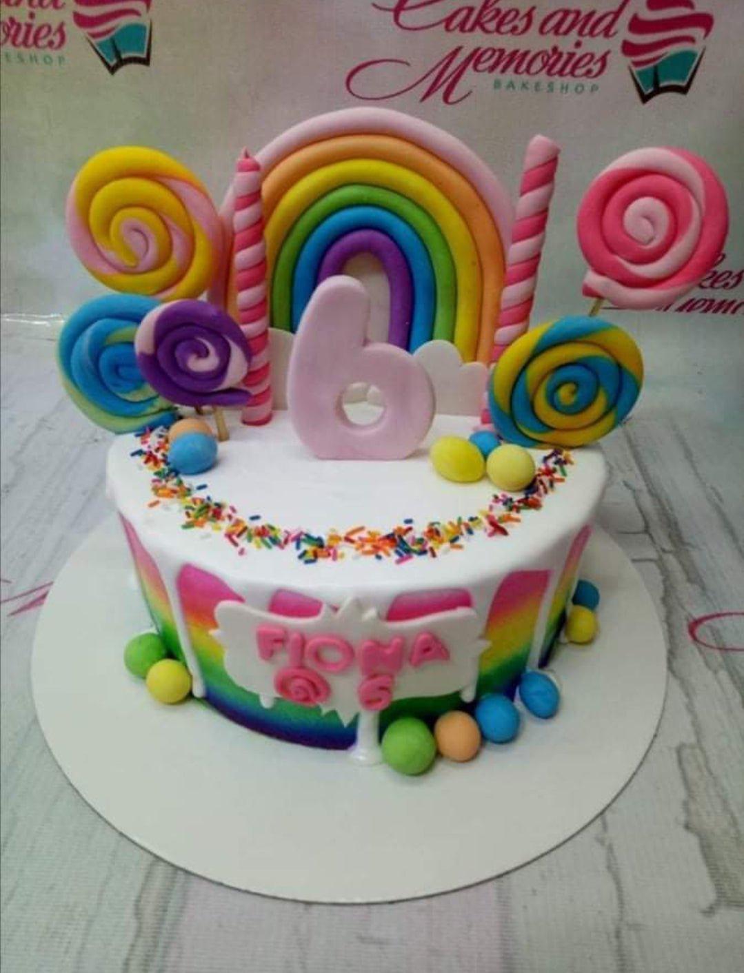 Colorful rainbow candy themed birthday cake with fondant lollipops, a large number 6, and rainbow arch on white icing.