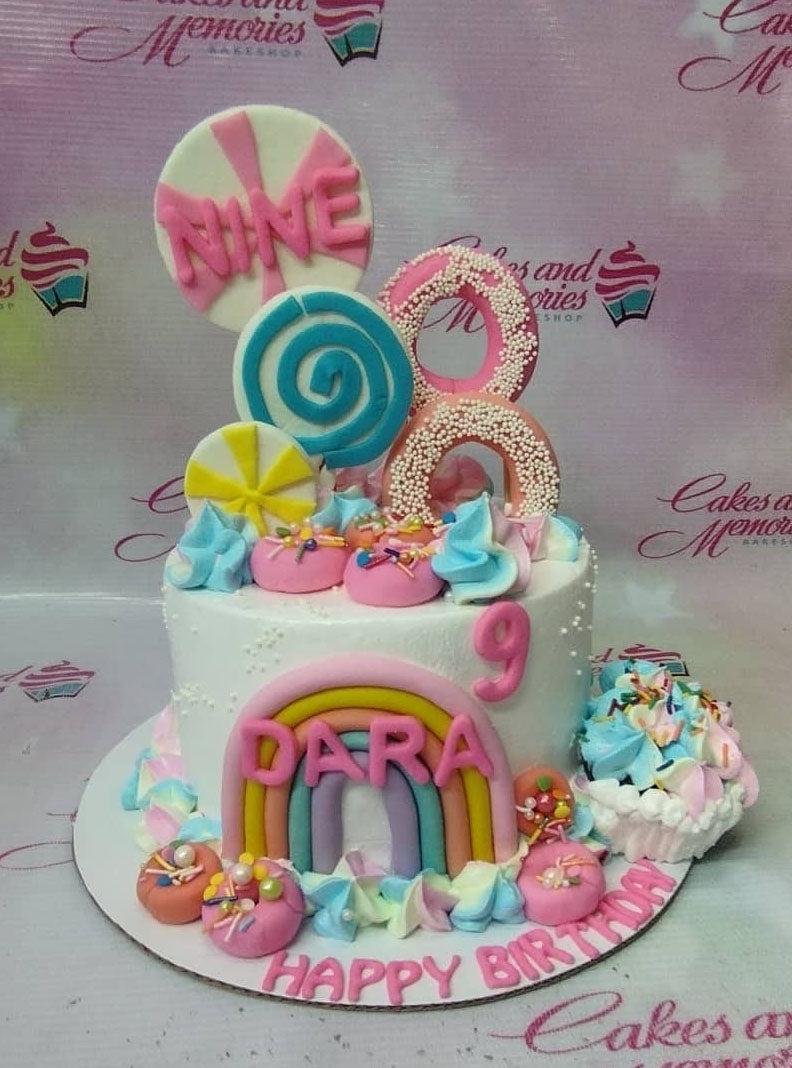 White 1-tier birthday cake with pink rainbow, donut toppers, and colorful icing swirls for Dara's 9th birthday.