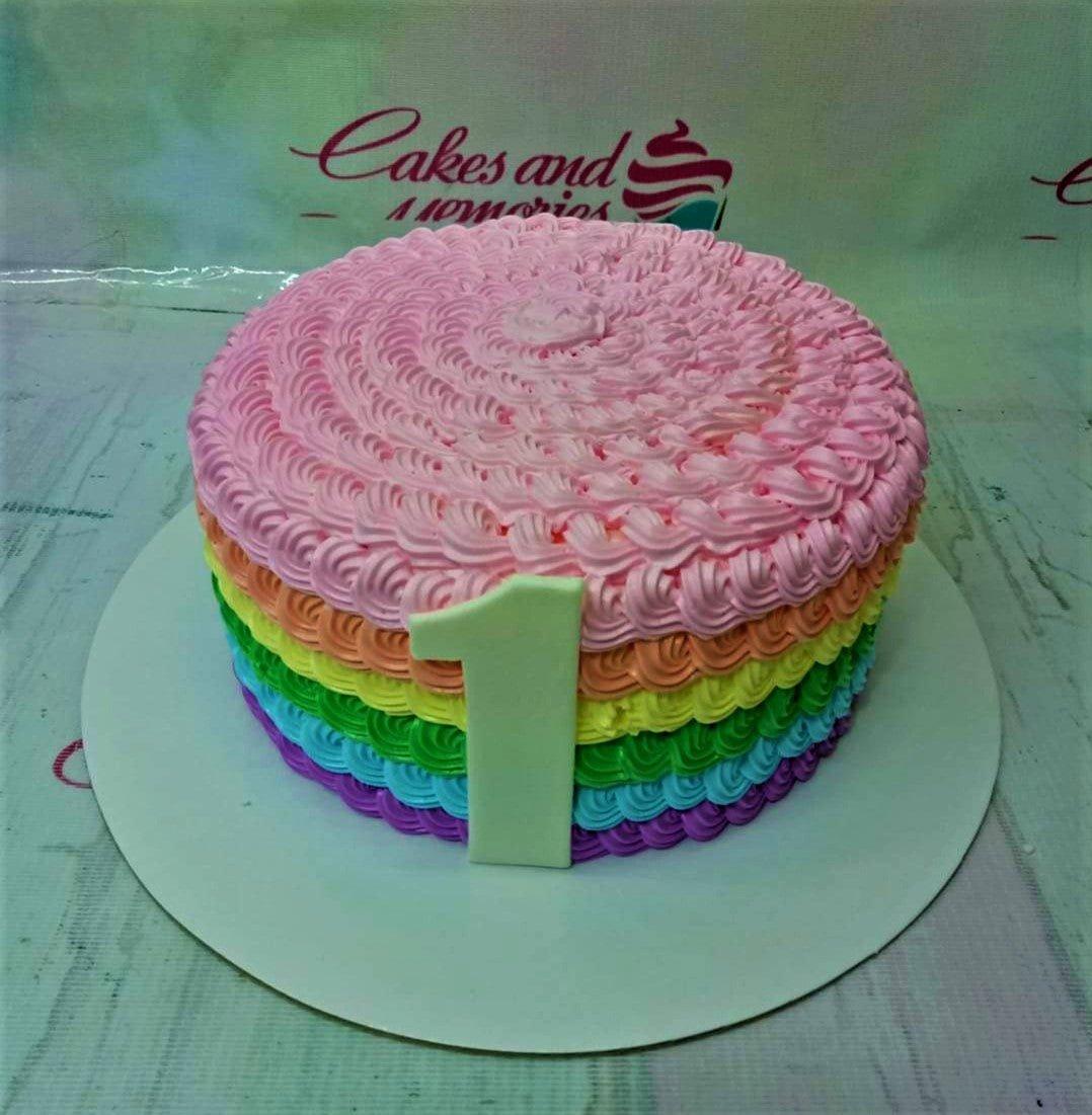 Rainbow layered icing cake with pink rosette top and a large light green number one fondant topper.