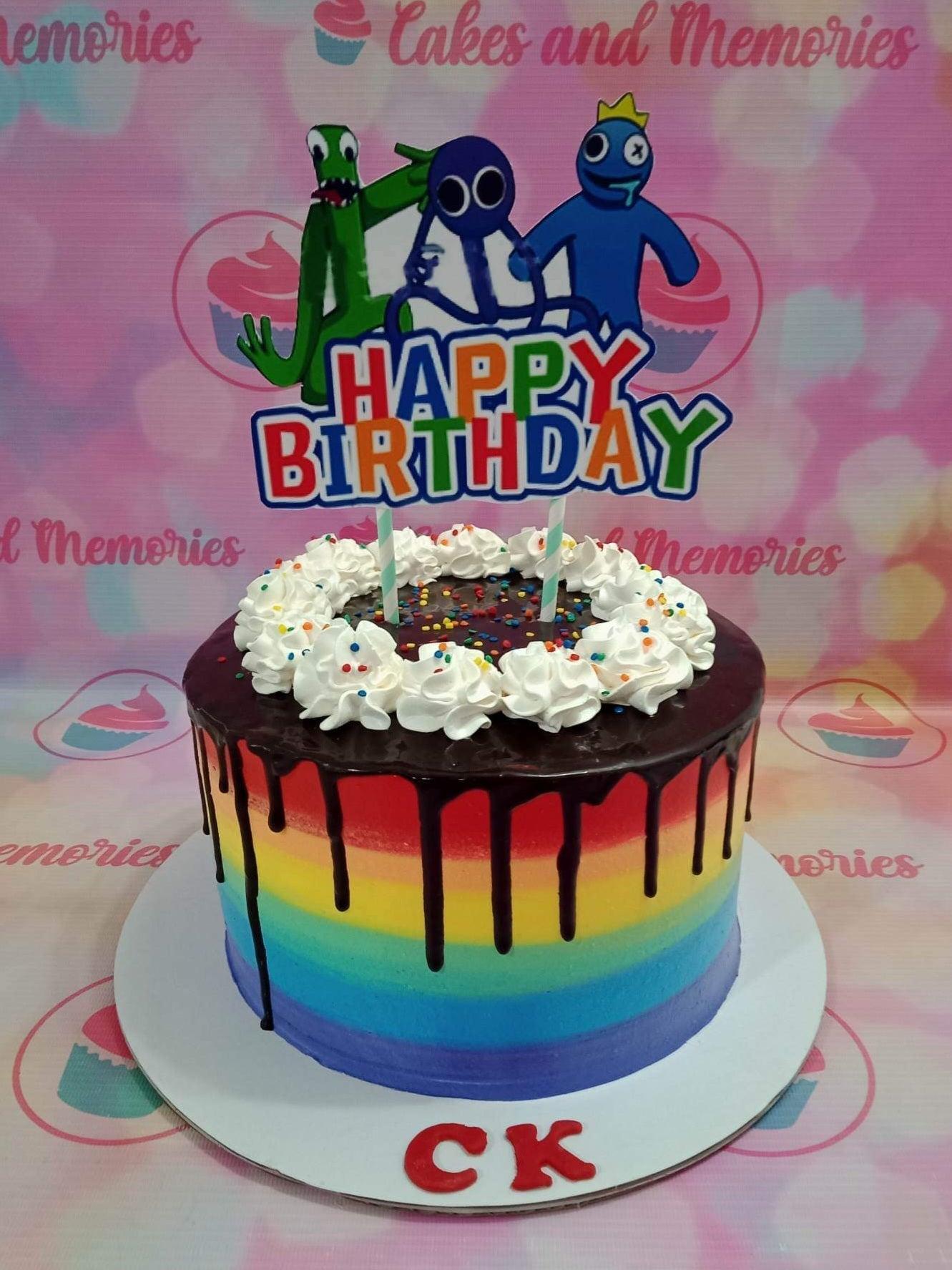 Rainbow striped birthday cake with chocolate drip, white icing swirls, and Rainbow Friends character toppers.