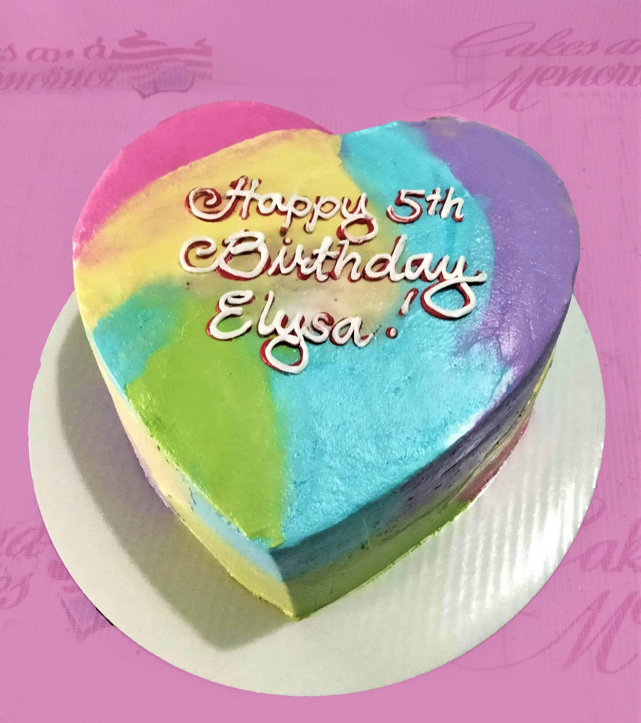 Heart-shaped bento cake with vibrant rainbow watercolor icing and white piped birthday message for Elysa.
