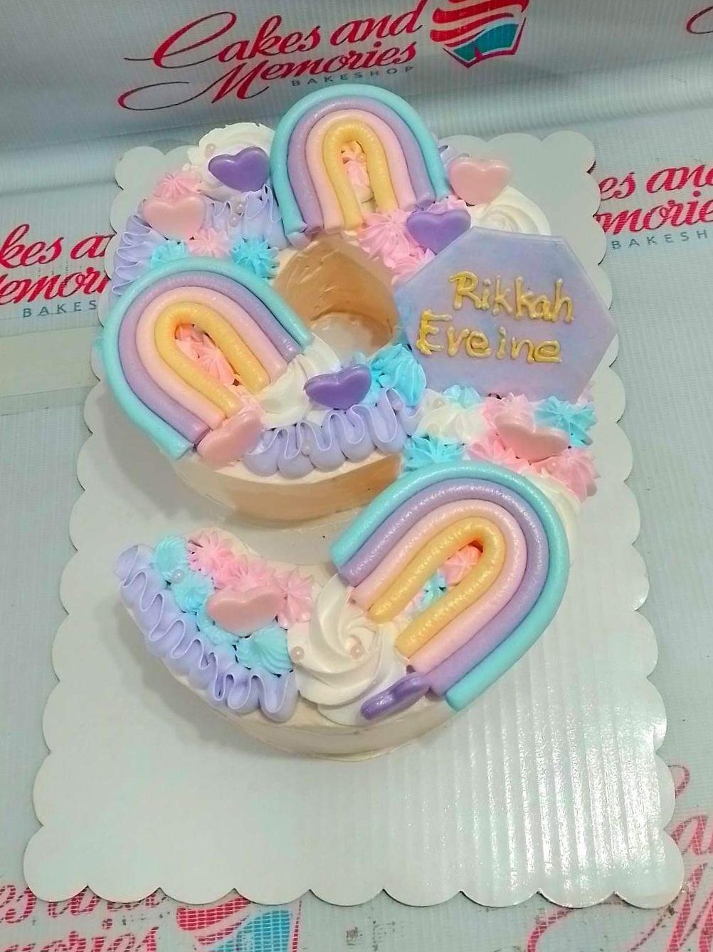 Number 3 shaped cake with pastel rainbow toppers, pink and purple hearts, and colorful icing rosettes.