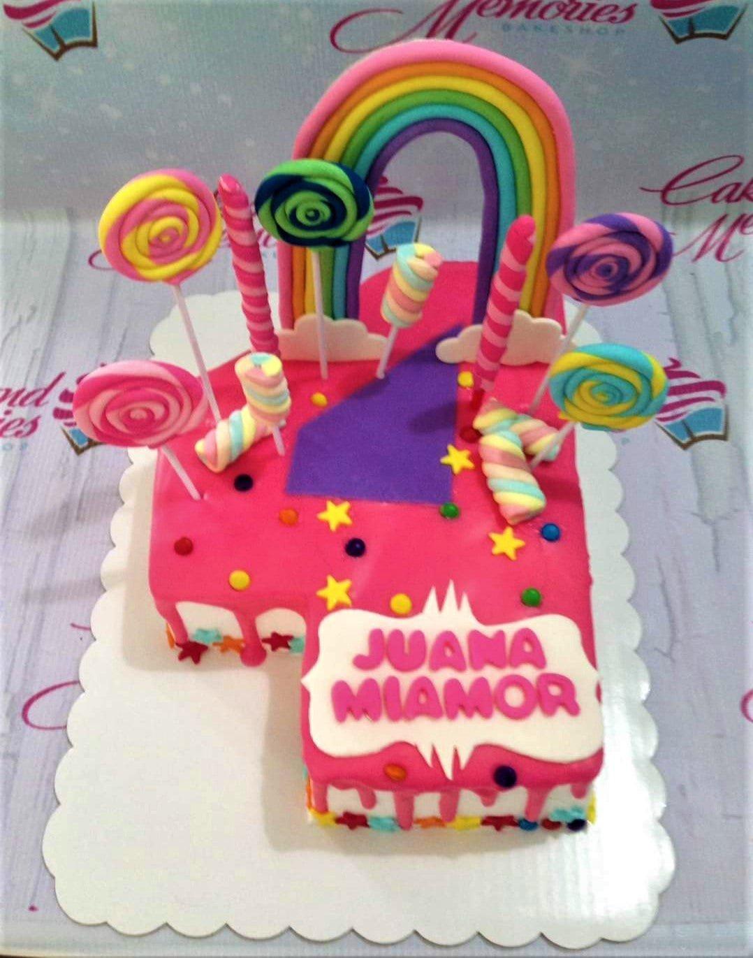 Number 4 shaped pink cake with a fondant rainbow, colorful lollipops, and marshmallow twists.