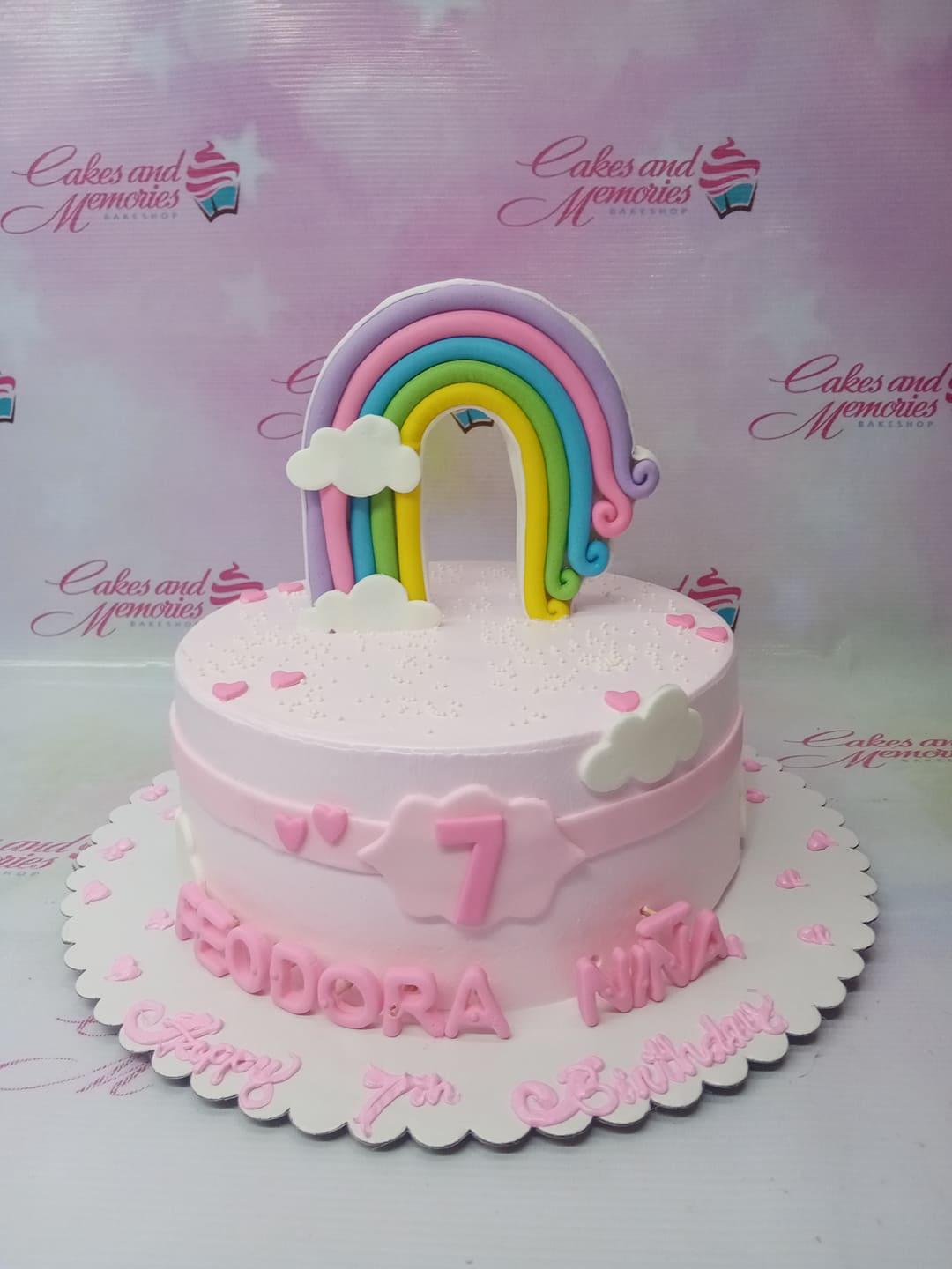 Pink rainbow birthday cake with fondant clouds, hearts, and a colorful rainbow topper for a 7th birthday celebration.