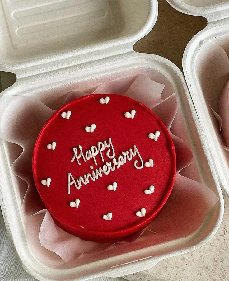 Red minimalist bento cake with white piped icing hearts and Happy Anniversary message in a white takeout container.