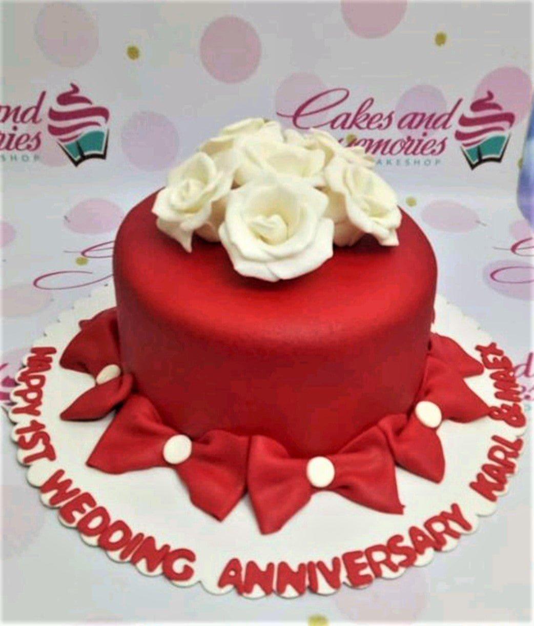 Red fondant anniversary cake with white edible roses on top and red fondant bows around the base.