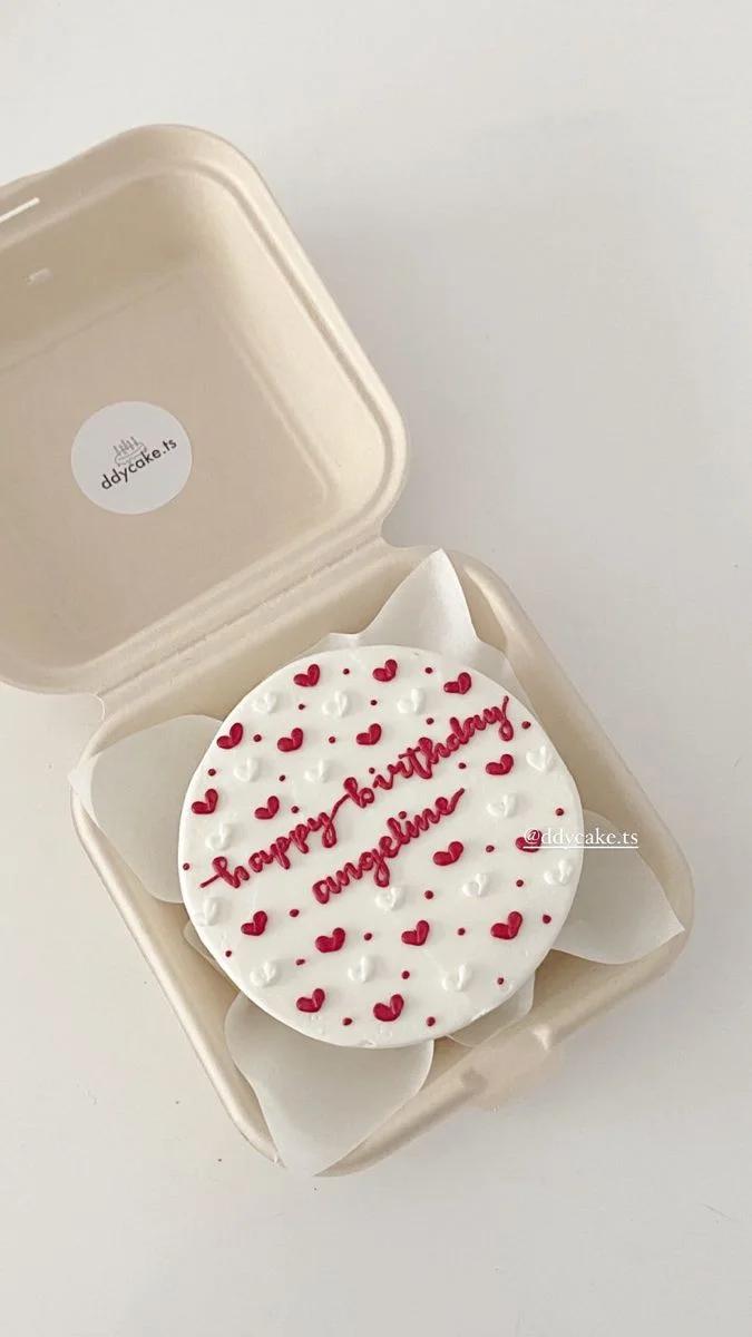White bento cake with red and white piped icing hearts and 'happy birthday angeline' message in red script.