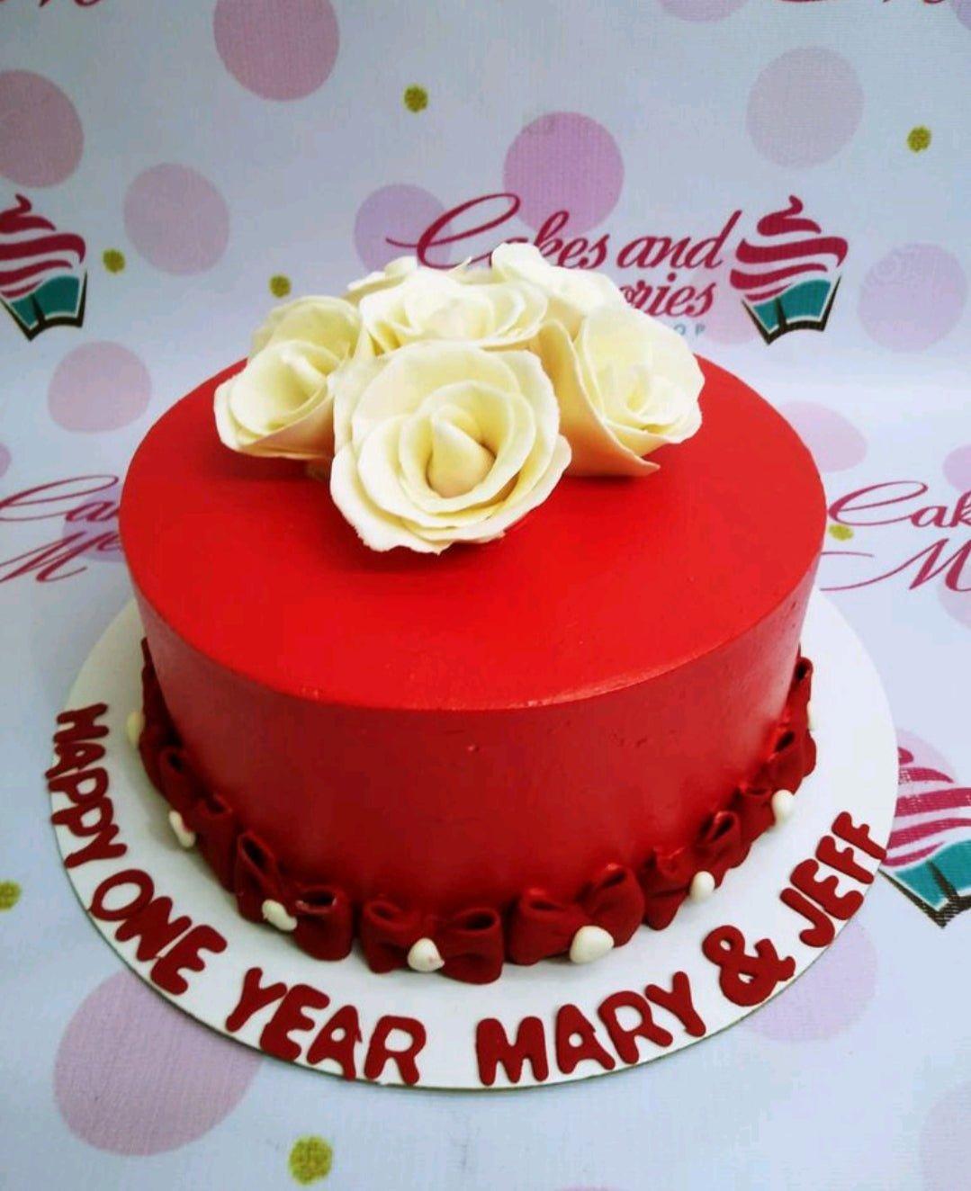 Red minimalist anniversary cake with white gumpaste roses and red fondant bows around the base.