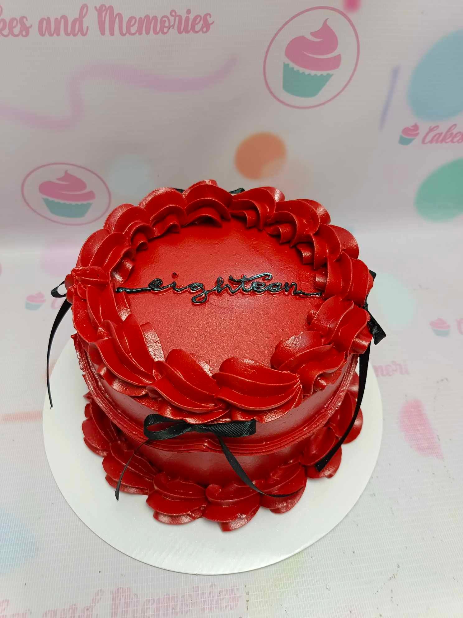 Deep red minimalist cake with ruffled icing borders, black ribbons, and a black 'eighteen' message on top.