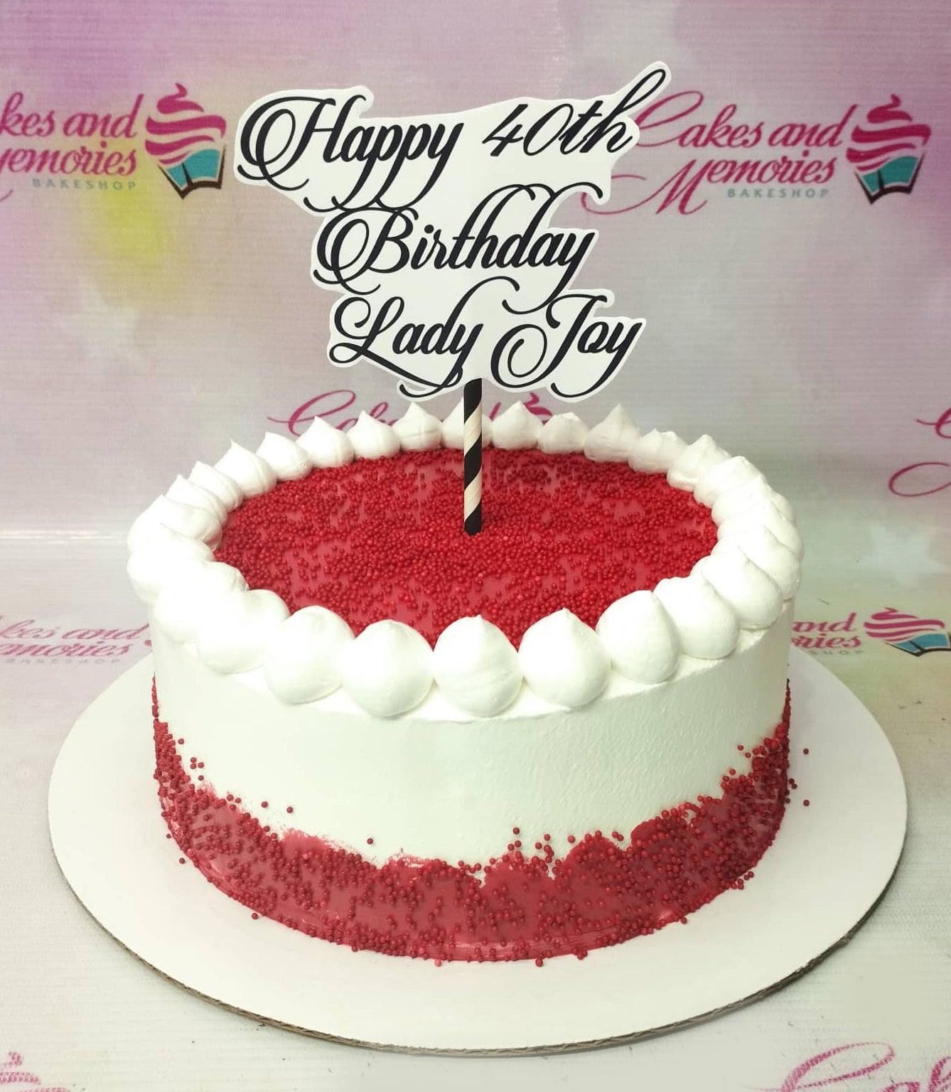White round cake with red sprinkles on top and bottom edge, featuring a large black and white Happy 40th Birthday Lady Joy topper.