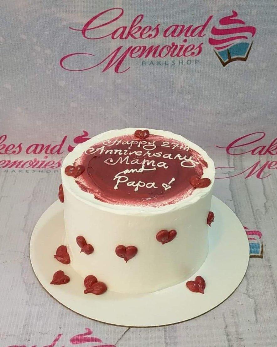White minimalist anniversary cake with a dark red painted icing top and piped red hearts on the sides.