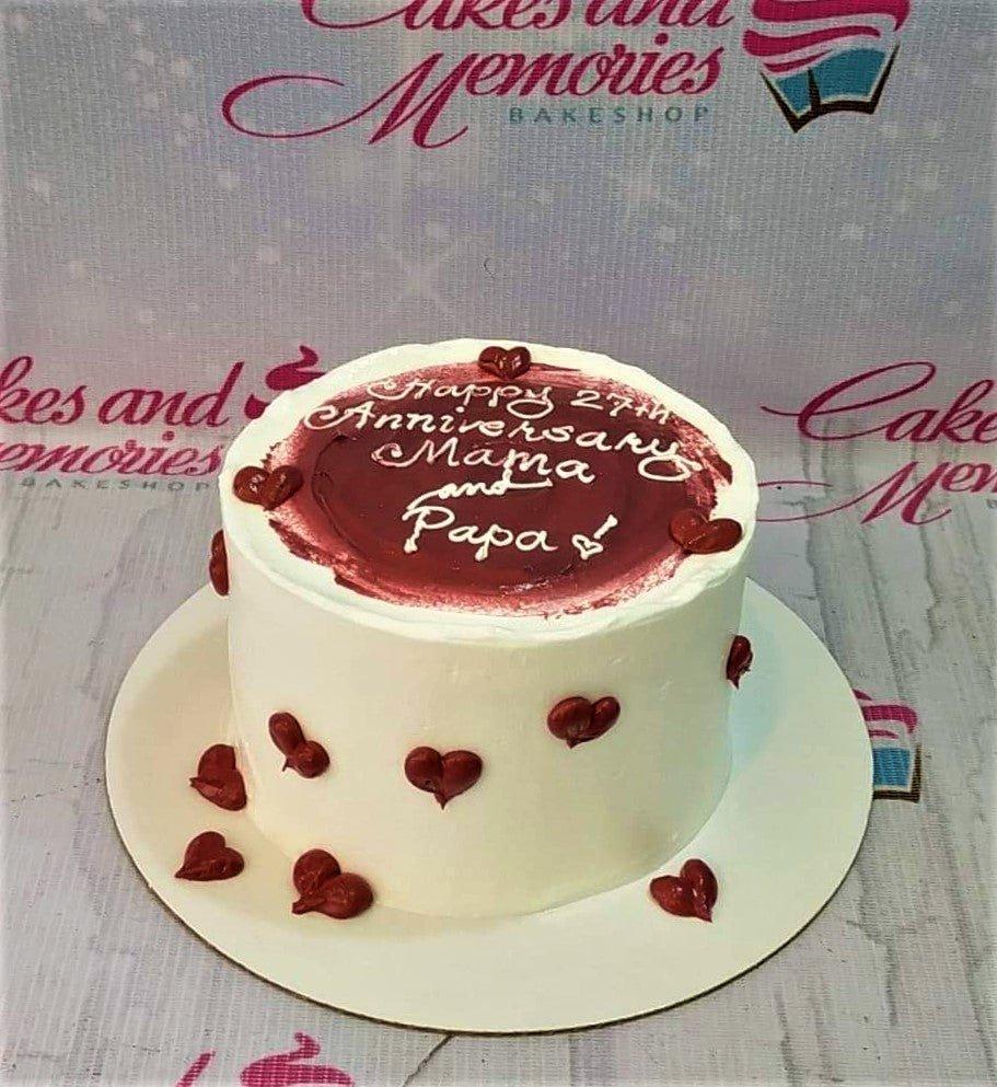 White minimalist anniversary cake with a deep red painted icing top and small red icing hearts on the sides.