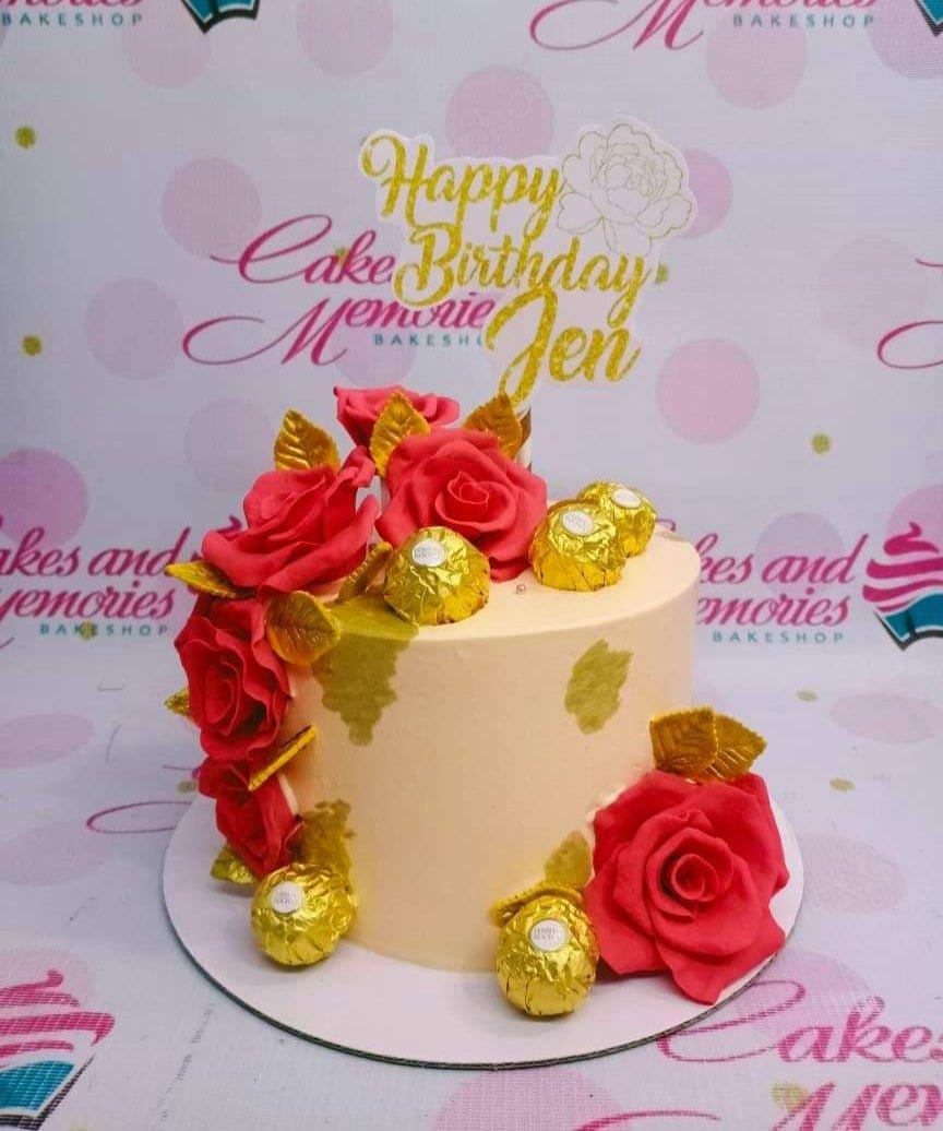 Peach 1-tier birthday cake decorated with large red gumpaste roses, gold leaves, and Ferrero Rocher chocolates with a gold glitter topper.