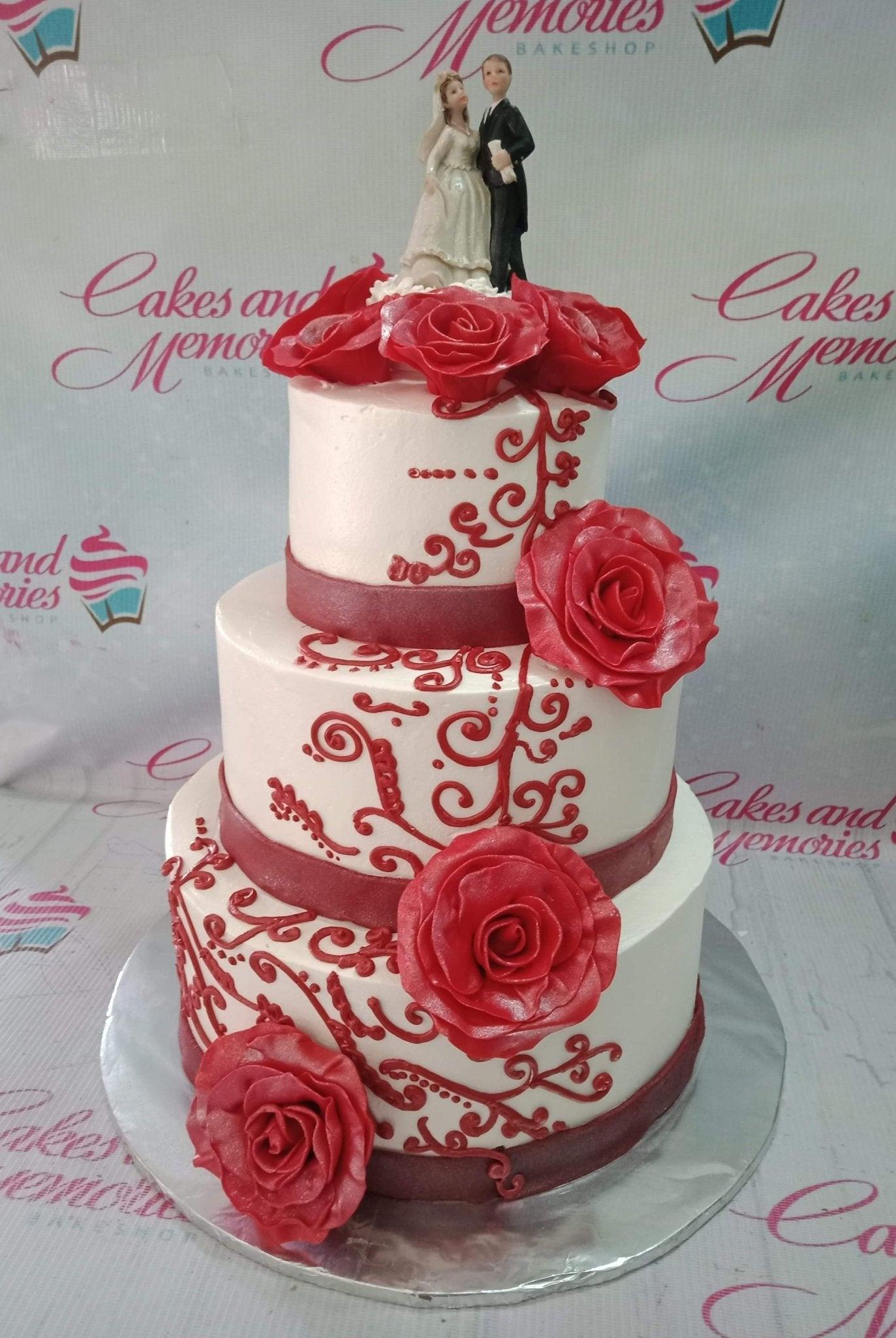 Elegant 3-tier white wedding cake with red icing roses and intricate red scrollwork piping on each tier.