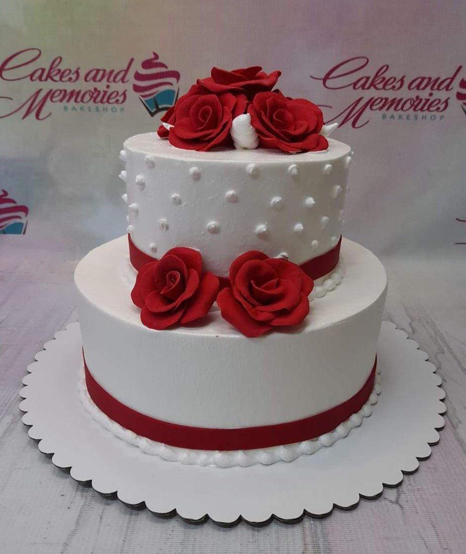 Elegant two-tier white cake decorated with vibrant red fondant roses and white icing dots.