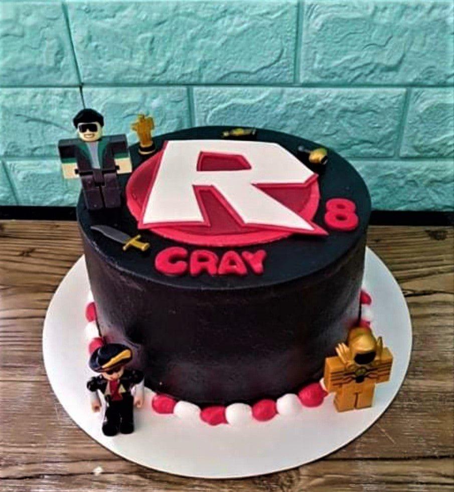 Black Roblox themed birthday cake with red and white icing borders, featuring a large R logo and character figurines.