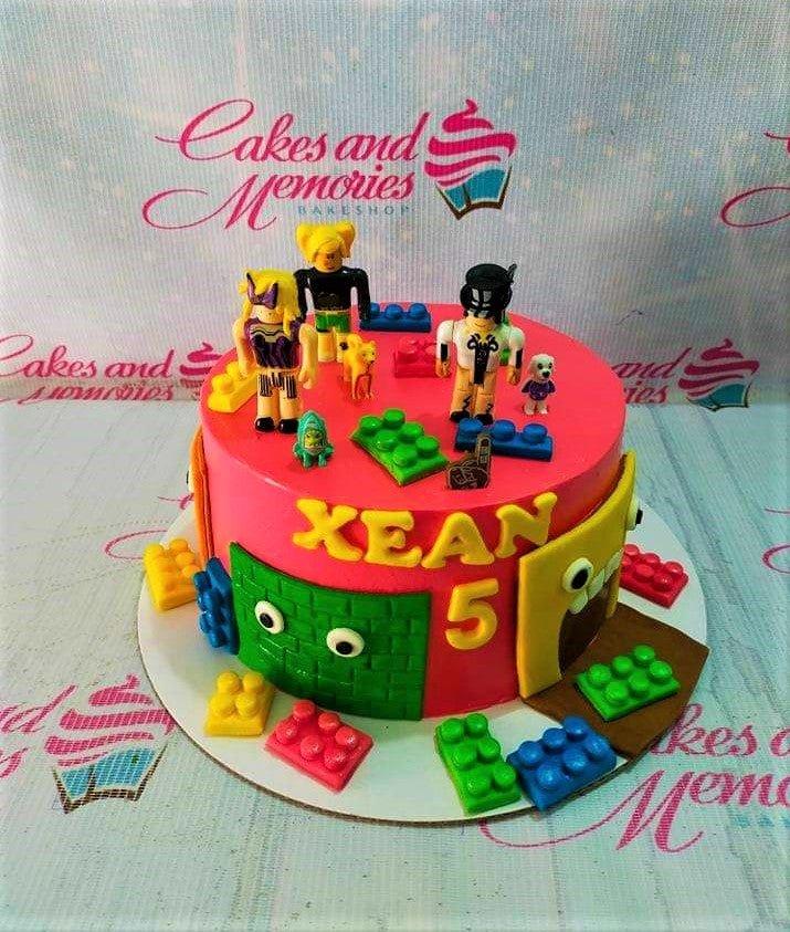Pink Roblox and Lego themed birthday cake with 3D fondant characters and colorful edible building blocks.